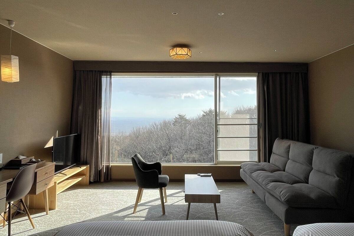 Une chambre d’hôtel moderne dotée d’une grande fenêtre, d’un canapé, d’un bureau et d’une chaise.