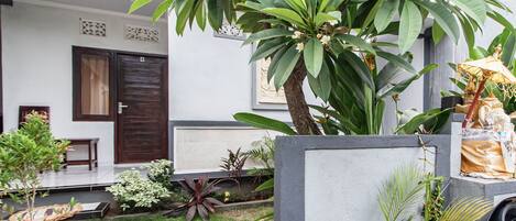 A garden area with a variety of plants and a small statue. There is a door and a window visible in the background.