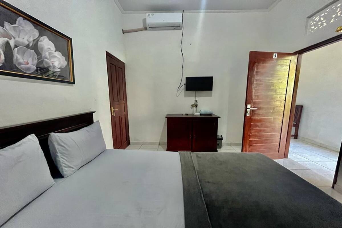 A hotel room with a bed, a TV mounted on the wall, a wooden door, and a small cabinet.