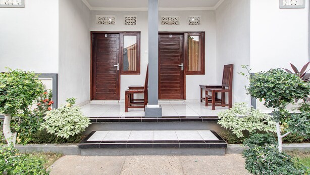 Una casa con porche cubierto, dos puertas de madera y un pequeño jardín con plantas.