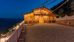A wooden lodge with a balcony, a stone wall, and a gravel driveway. - The Oaknut Cottage Birding Lodge (Kosiyakutoli)