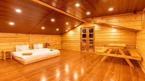 A wooden cabin room with a bed, a bench, and a door leading to a loft area. - The Oaknut Cottage Birding Lodge (Kosiyakutoli)