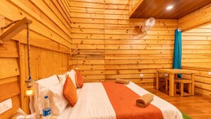 A wooden cabin room with a bed, a table, and a fan. - The Oaknut Cottage Birding Lodge (Kosiyakutoli)