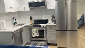 Una cocina moderna con armarios blancos, electrodomésticos de acero inoxidable y un sofá azul al frente.