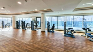 Ein geräumiger Fitnessraum mit verschiedenen Trainingsgeräten, großen Fenstern und Blick auf die Stadt sowie einem glatten Holzboden.