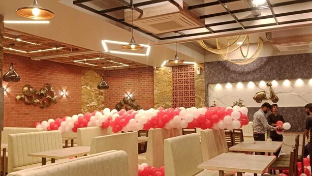 A restaurant with a brick wall, marble columns, and tables with white and red balloons. - Hotel SAP (Kalol)