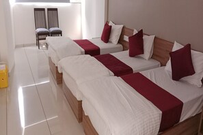 A hotel room with three beds, each with white bedding and red accents. There are two wooden chairs against the wall and a small yellow trash bin. - Hotel SAP (Kalol)