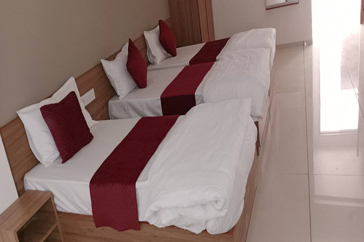 A hotel room with three beds, each with white bedding and red accents.