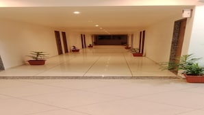 A long, well-lit hallway with tiled floors and potted plants along the sides. - Hotel SAP (Kalol)