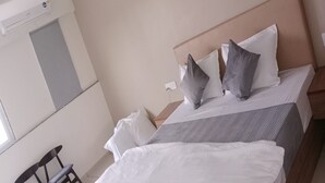 A neatly made bed with white and gray bedding, a wooden headboard, and a small bedside table. - Hotel SAP (Kalol)