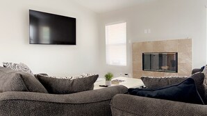 A modern living room with a flat-screen TV mounted on the wall, a fireplace, and a large sectional sofa.