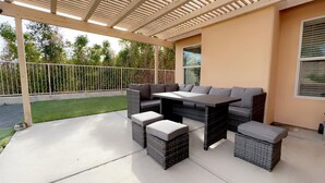 An outdoor patio with a wicker sofa set, a table, and cushioned footrests.
