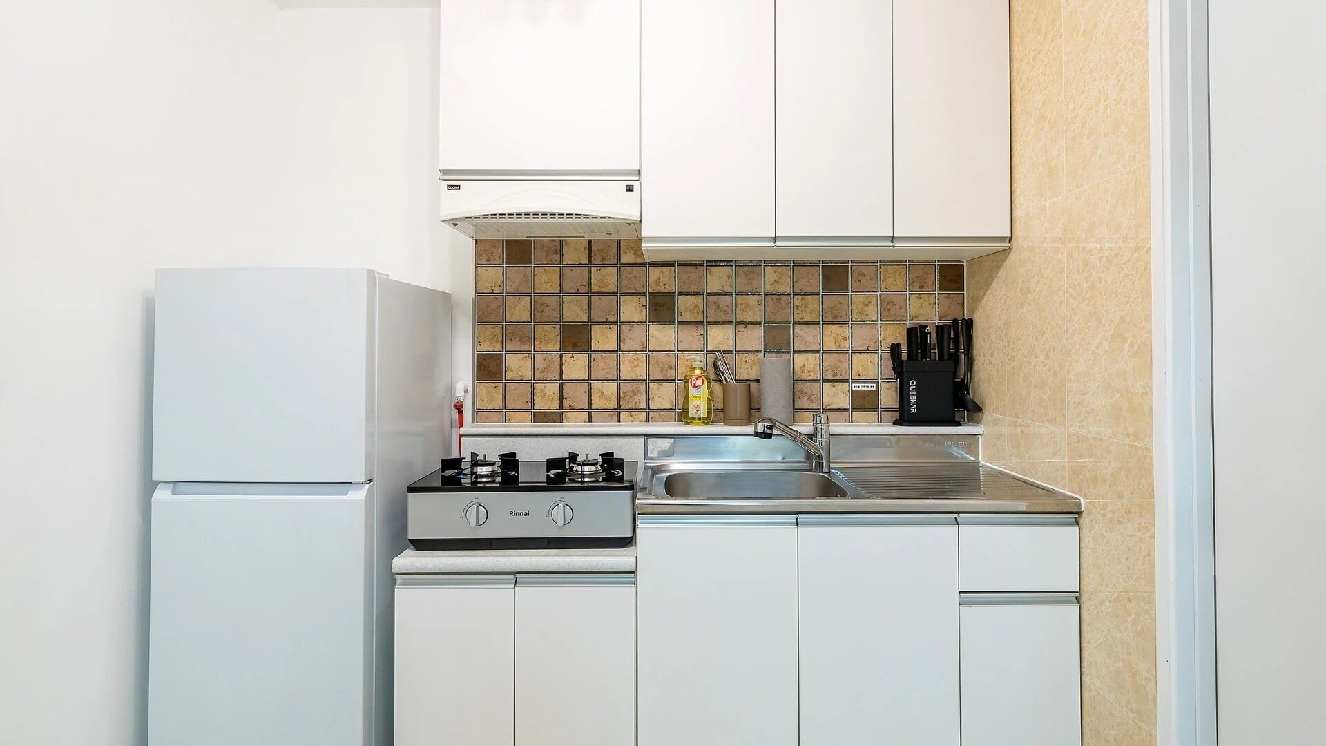 Uma cozinha compacta com armários brancos, fogão a gás, pia e painel de azulejos.
