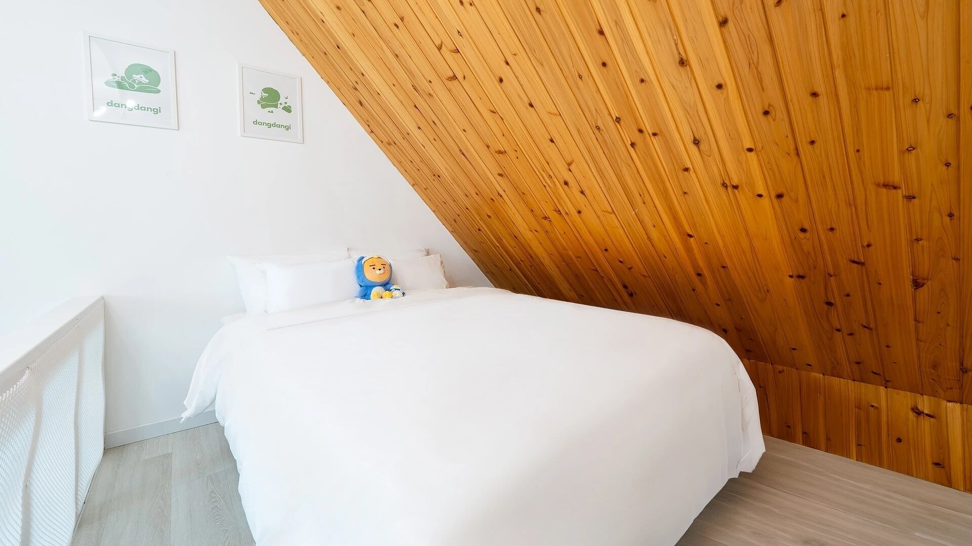 A bedroom with a sloped ceiling, a bed, a plush toy, and two framed pictures on the wall.