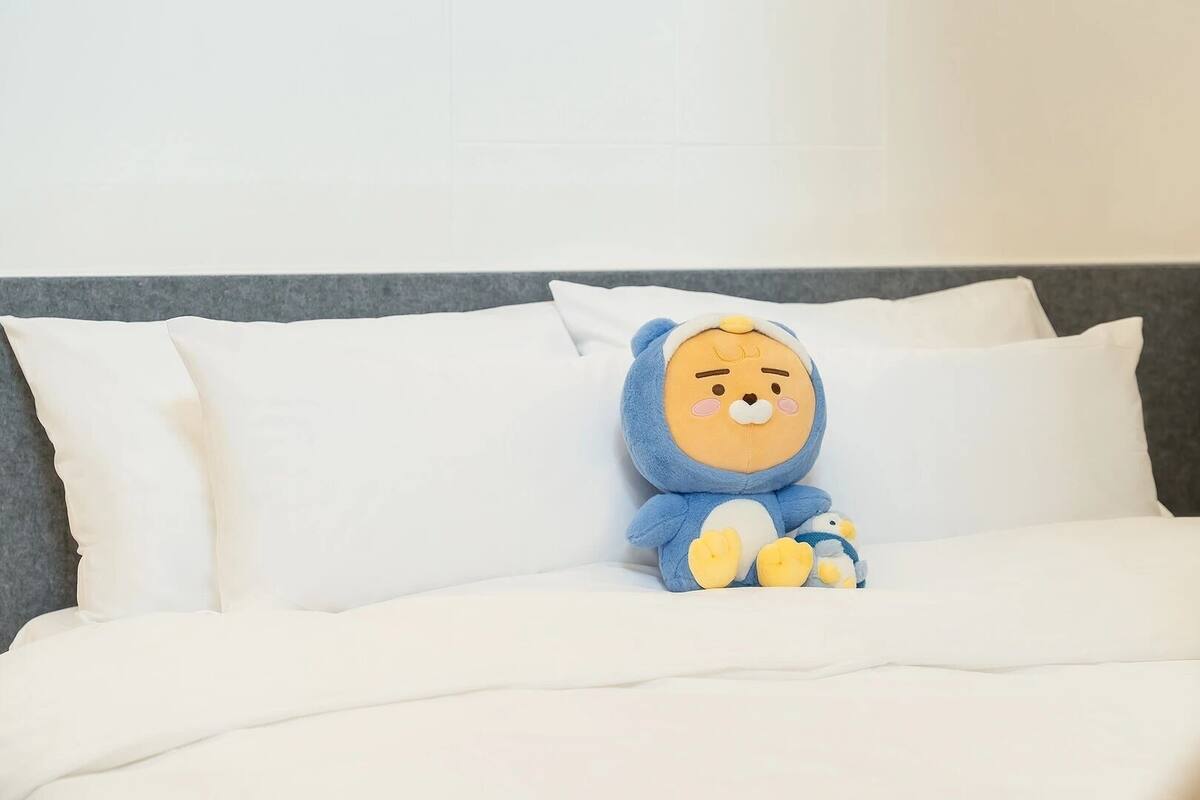 Un lit avec une literie blanche et un jouet en peluche posé dessus.