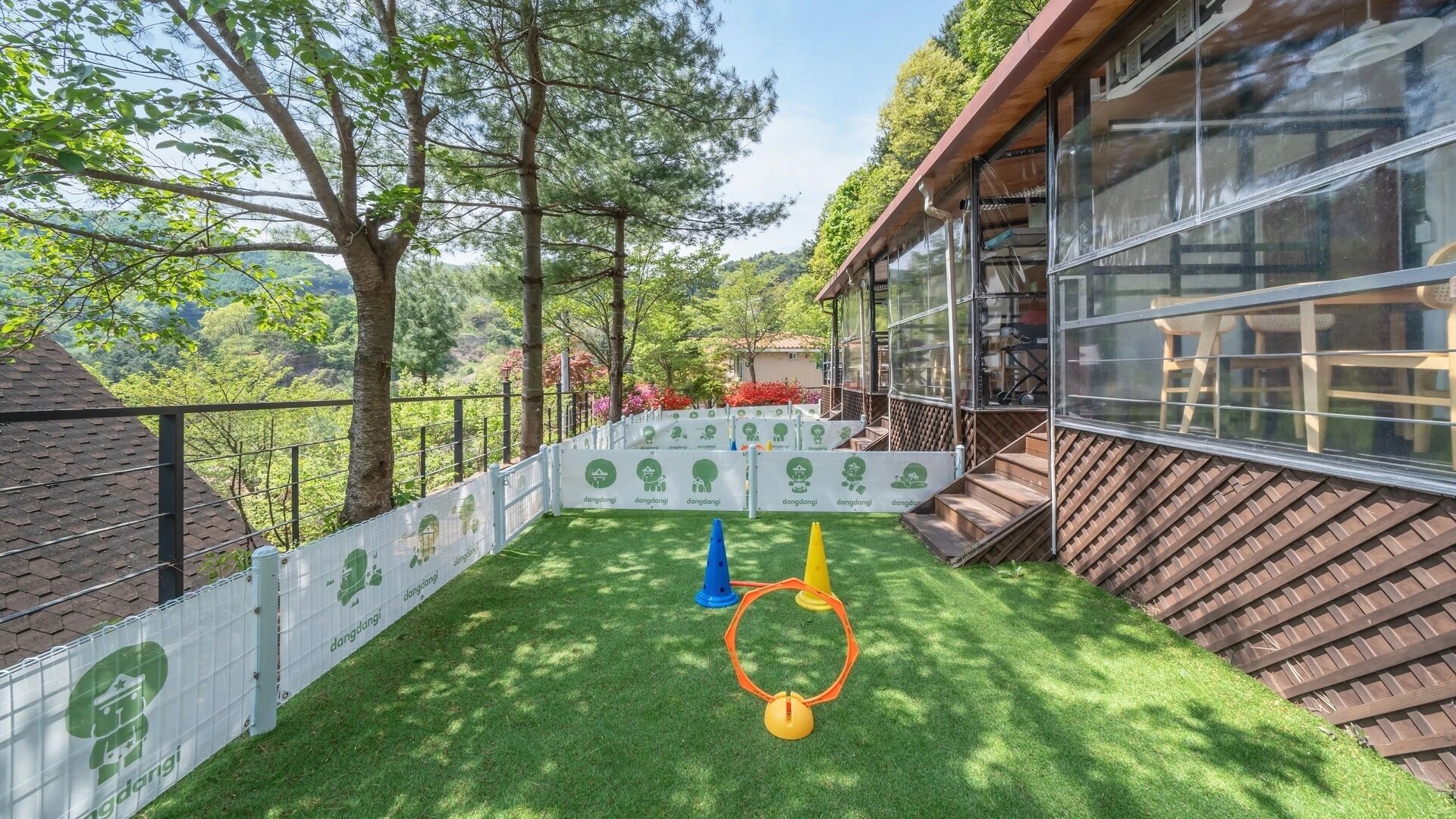 A backyard with artificial grass, a wooden deck, and a white fence with green logos.