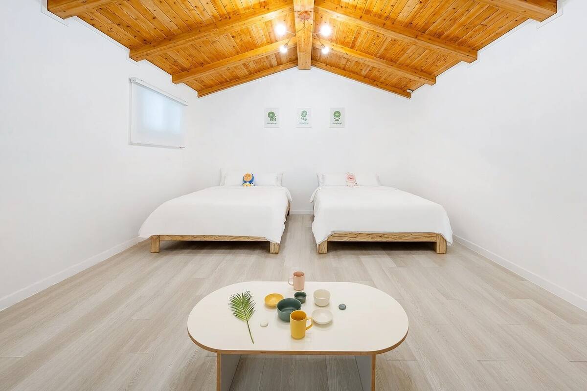 Une pièce avec deux lits, une table avec des tasses et une plante, et un plafond en bois.