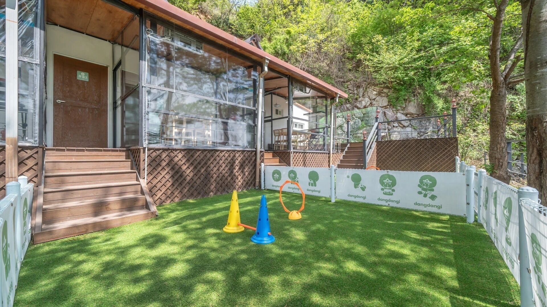 Un bâtiment à l’extérieur en bois, doté de grandes fenêtres et d’une cour verdoyante avec des jeux pour enfants.