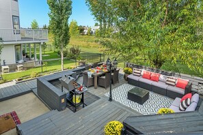 Une terrasse dotée de mobilier d’extérieur, d’un barbecue et offrant une vue sur une pelouse verdoyante et des arbres.
