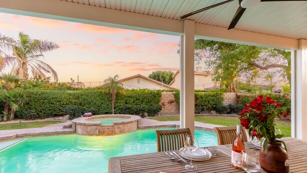 A poolside dining area with a table set for two, a pool, and a sunset view.
