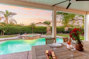 A poolside dining area with a table set for two, a pool, and a sunset view.