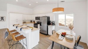 A modern kitchen with white cabinets, stainless steel appliances, a central island, and a dining area with a wooden table and chairs.