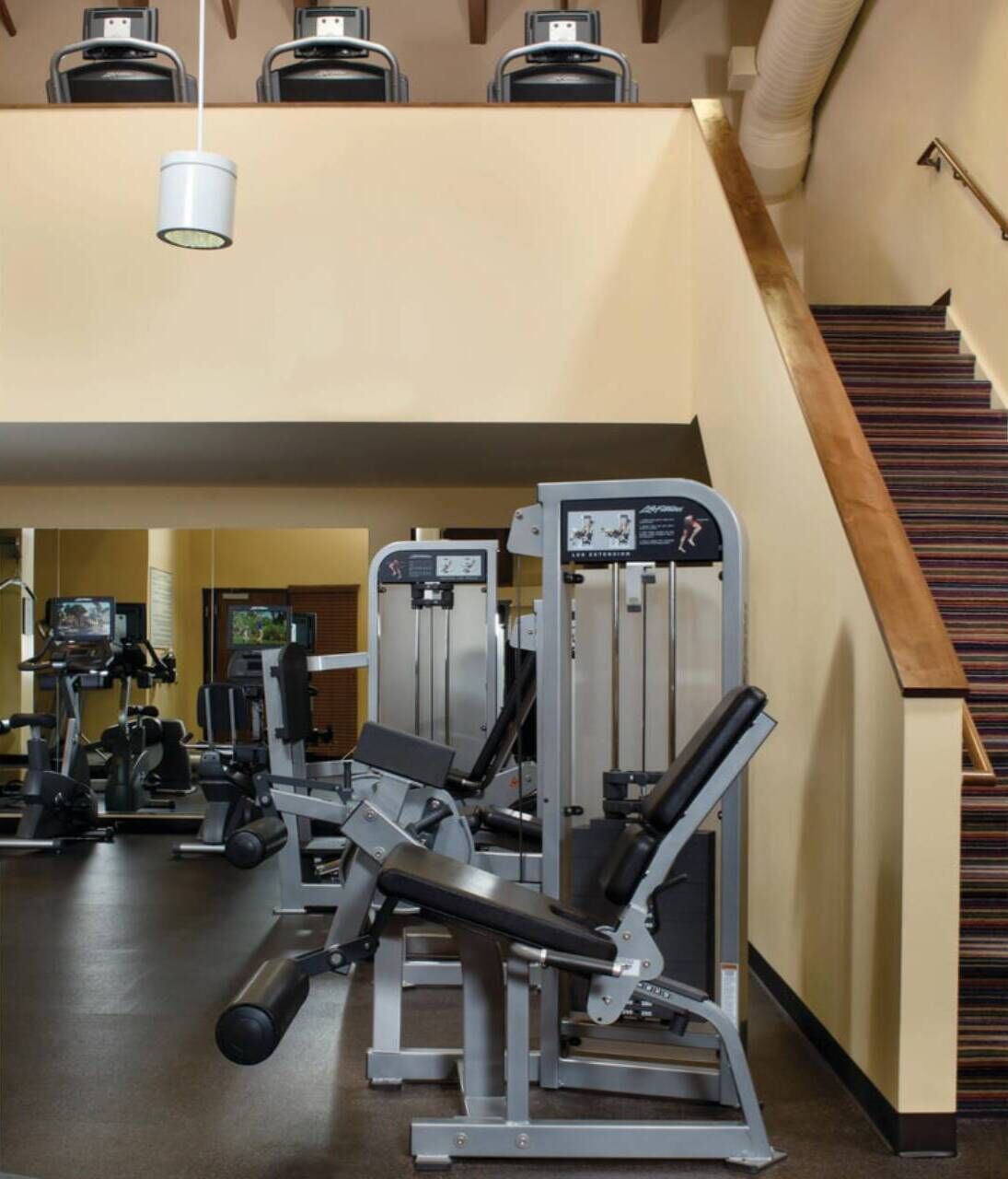A gym with various exercise machines, a television, and a staircase.