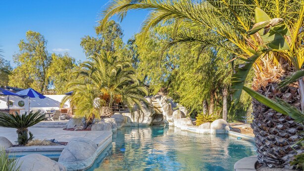 A swimming pool surrounded by tropical plants and rocks. - Expansive Wine Country Estate | Pool + Hot Tub | Sleeps 20 | Quiet Retreat (Temecula)