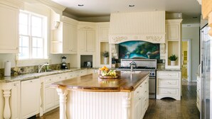 A spacious kitchen with a large island, white cabinetry, and a painting above the stove. - Expansive Wine Country Estate | Pool + Hot Tub | Sleeps 20 | Quiet Retreat (Temecula)