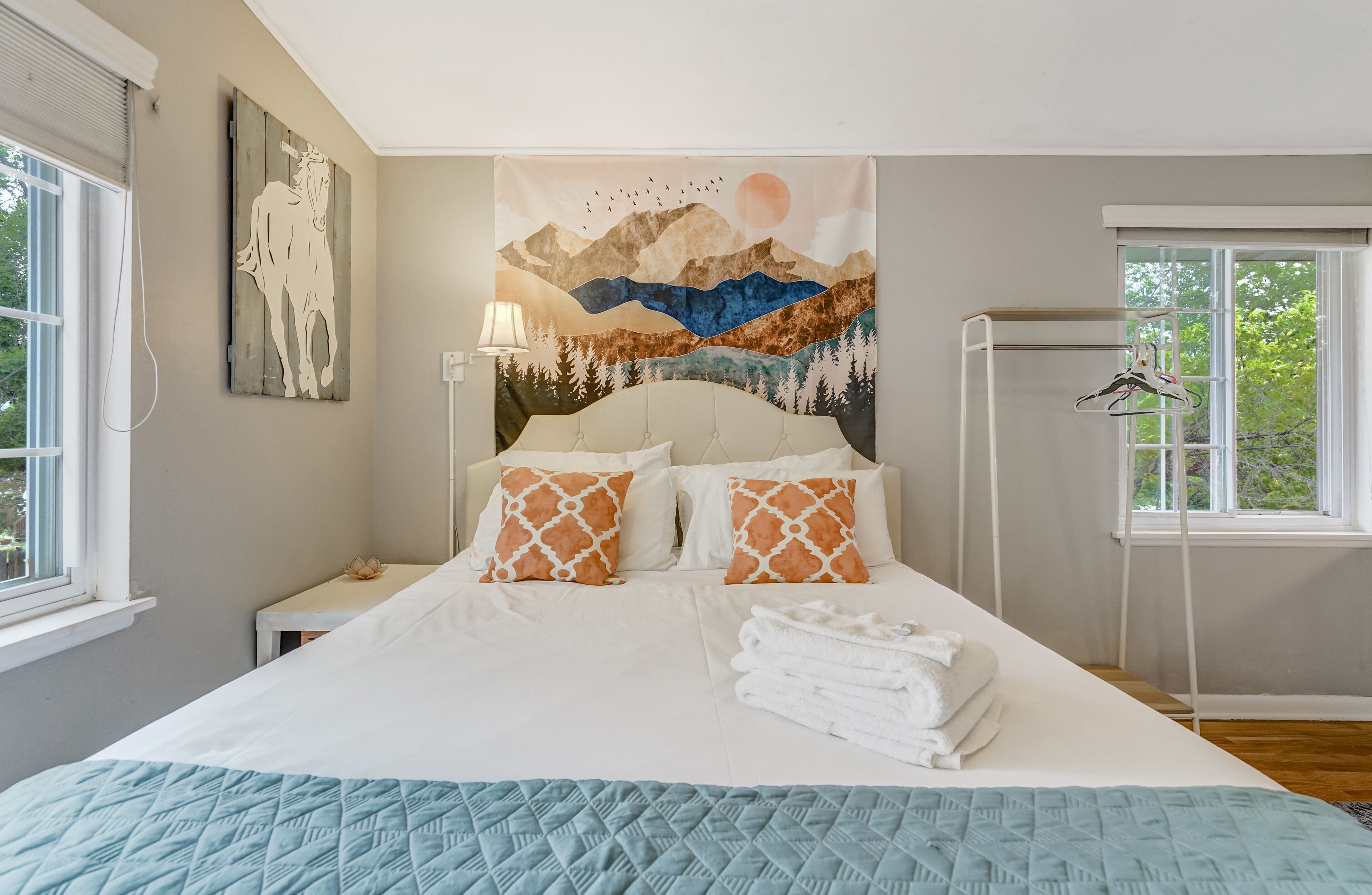 Ein Schlafzimmer mit einem Bett, Kissen, einem Nachttisch, einer Lampe, einem Fenster und Wandteppich.