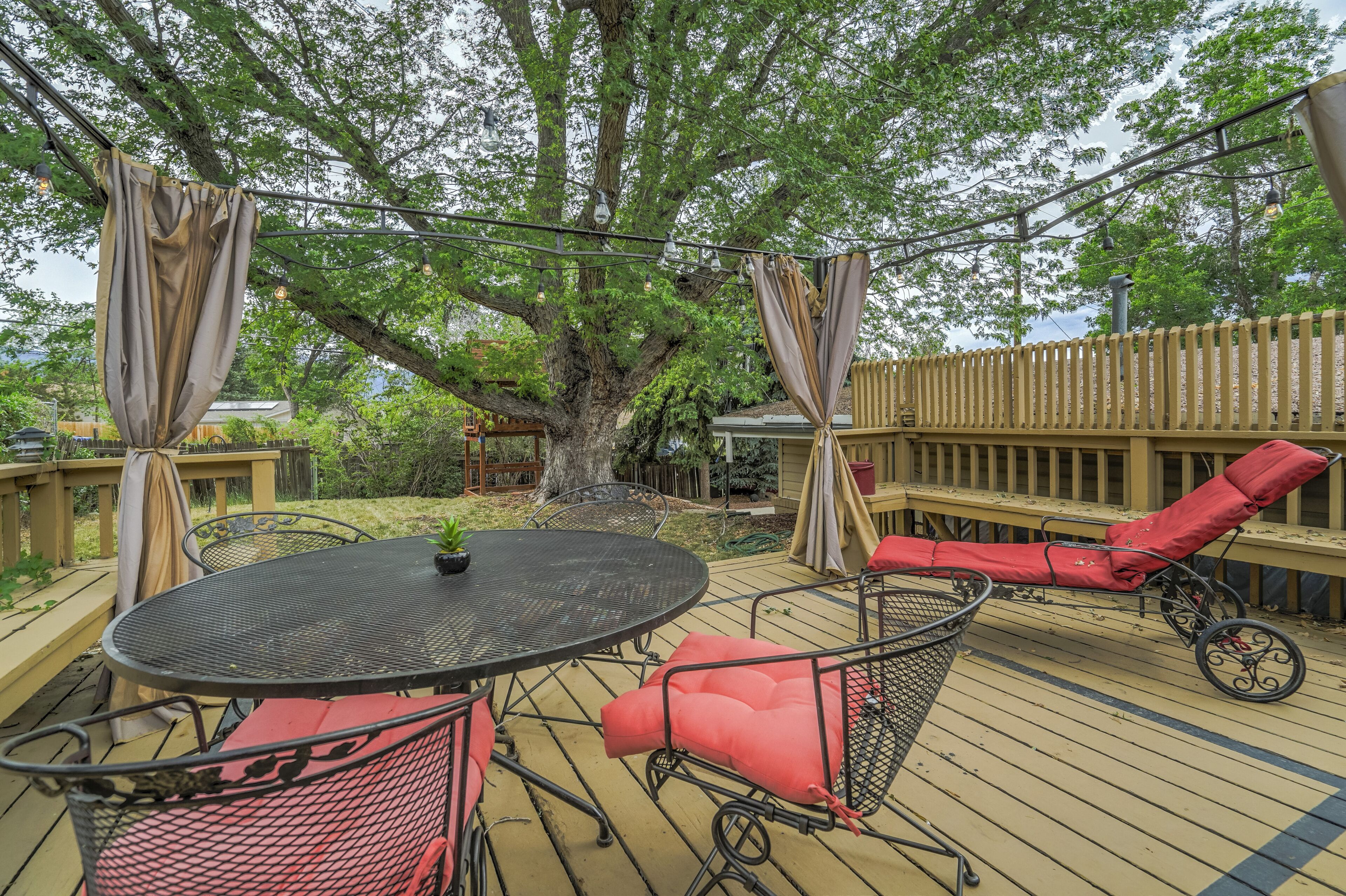 A deck with a round table and chairs, a red cushioned chair, and a canopy.
