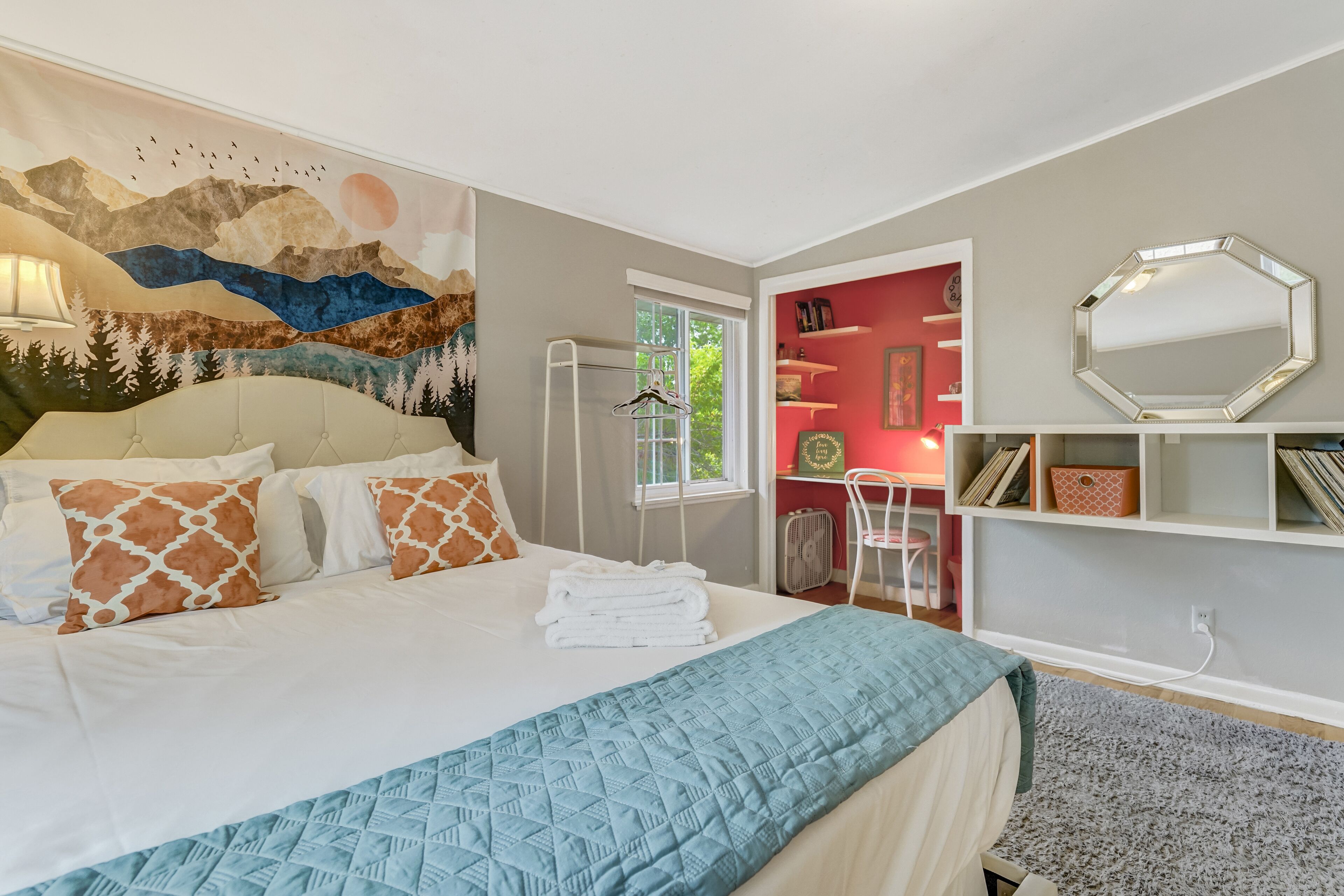A bedroom with a bed, a mural, a window, a desk, and a mirror.