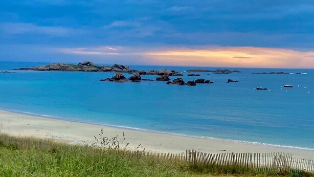 En strand med klart blåt vand, sand og spredte sten.