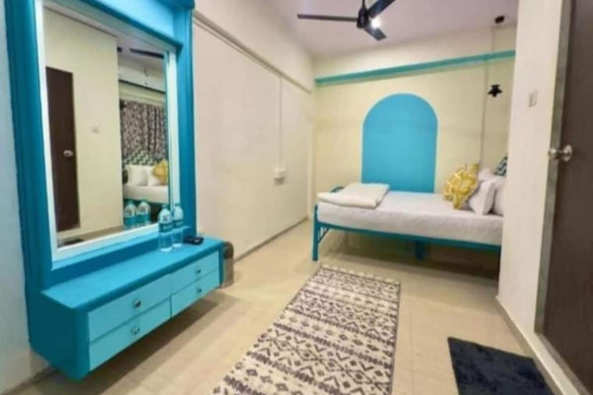 A bedroom with a large mirror, a bed with a blue headboard, a bedside table, and a patterned rug.