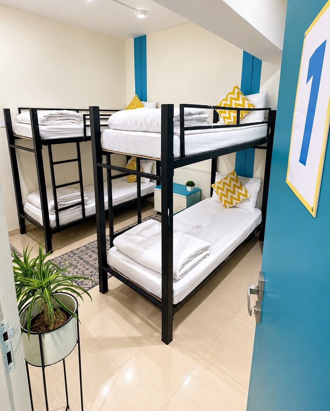 A bunk bed room with white bedding and yellow pillows, a small bedside table, and a potted plant.