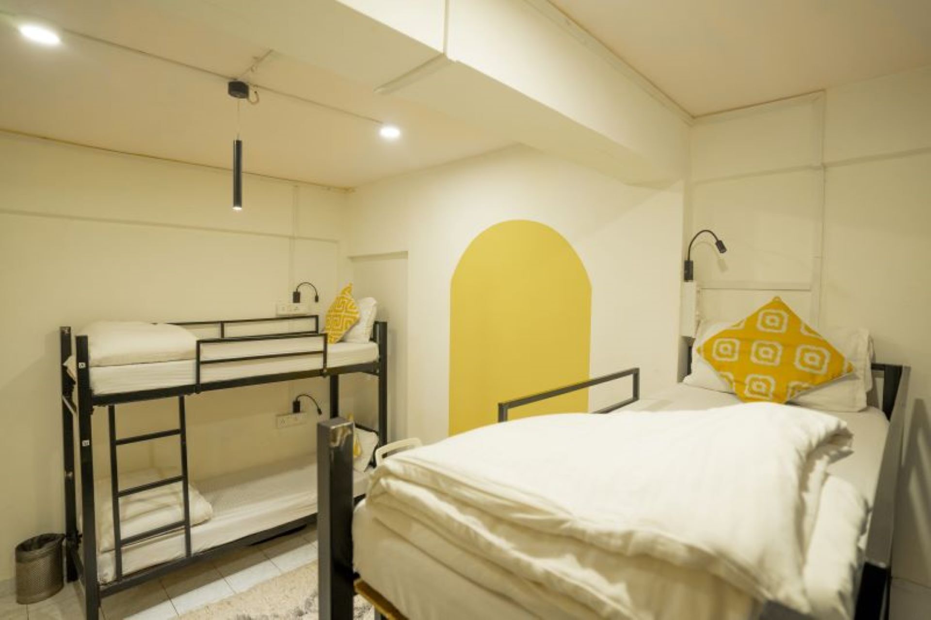 A dorm-style room with bunk beds, a single bed, and a yellow arch wall.