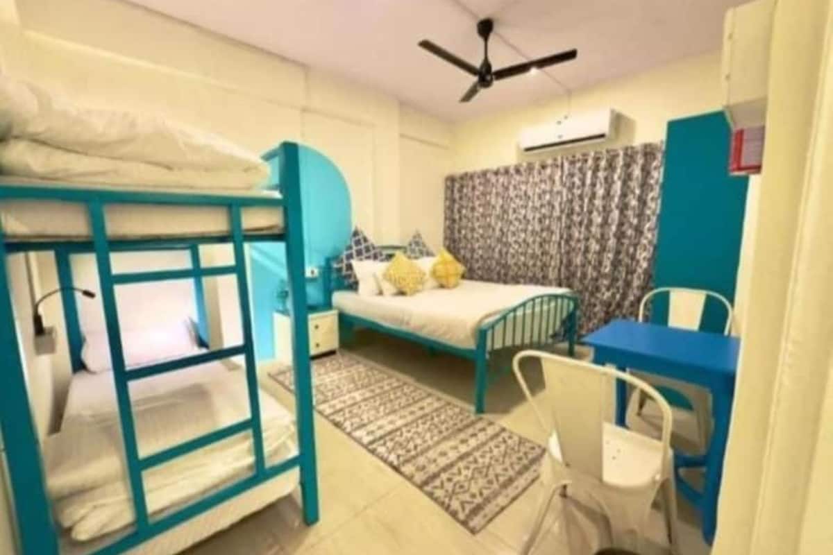 A dorm-style room with bunk beds, a desk, a chair, and a ceiling fan.