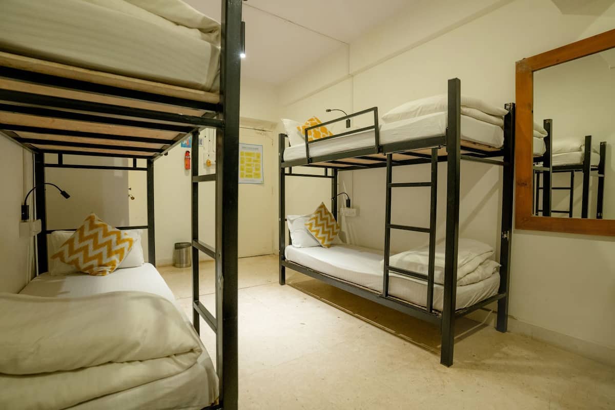 A dormitory room with bunk beds, a small trash bin, a fire extinguisher, and a mirror on the wall.