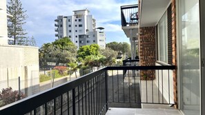 A balcony with a view of a residential area, including a multi-story building and trees.