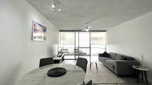 A modern living room with a grey sofa, a round table with a black object, and a ceiling fan.