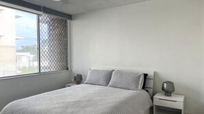 A bedroom with a bed, two bedside tables, and a window with a metal screen.