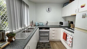 Una cocina moderna con encimera de granito, pileta de acero inoxidable, muebles blancos, microondas, tostadora y un reloj en la pared.