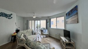 A spacious living room with a sofa, armchairs, a television, and a large window. - Chequers Caloundra U2, Walk To Kings & Shelly (KINGS BEACH)