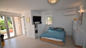 A bedroom with a bed, a TV, a wardrobe, and a sliding glass door leading to an outdoor area. - PRESQU'Île de GIENS STUDIO REZ-de-JARDIN villa Parc Résidentiel la POLYNESIE (Hyères)