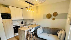 Een moderne keuken met houten kastjes, een eetgedeelte met een ronde tafel, en een zithoek met een bank en decoratieve muurkunst.