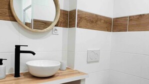 Een moderne badkamer met een witte wastafel, een zwarte kraan en een ronde spiegel.