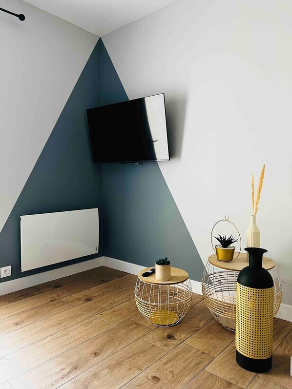 Una sala de estar moderna con un televisor de pantalla plana montado en la pared, un radiador, una mesa redonda de madera con una planta en maceta y dos jarrones decorativos.