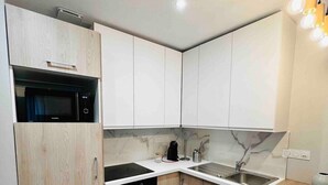 Een moderne keuken met witte kasten, een zwarte kookplaat, een inbouwmagnetron, een spoelbak en een houten aanrecht.