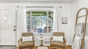 A room with two brown leather chairs, a small round table with a plant, and a window with white curtains. - Green Dream (Cascade)