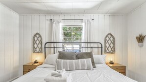 A neatly made bed with white linens, two bedside tables with lamps, and a window with curtains. - Green Dream (Cascade)